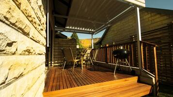 Eine Terrasse im Freien mit Holzboden, einem Grill und einem überdachten Sitzbereich mit Stühlen.