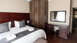 A hotel room with a large bed, a wooden wardrobe, a desk with drawers, and a mirror on the wall. - La Bri Self Catering (Clarens)