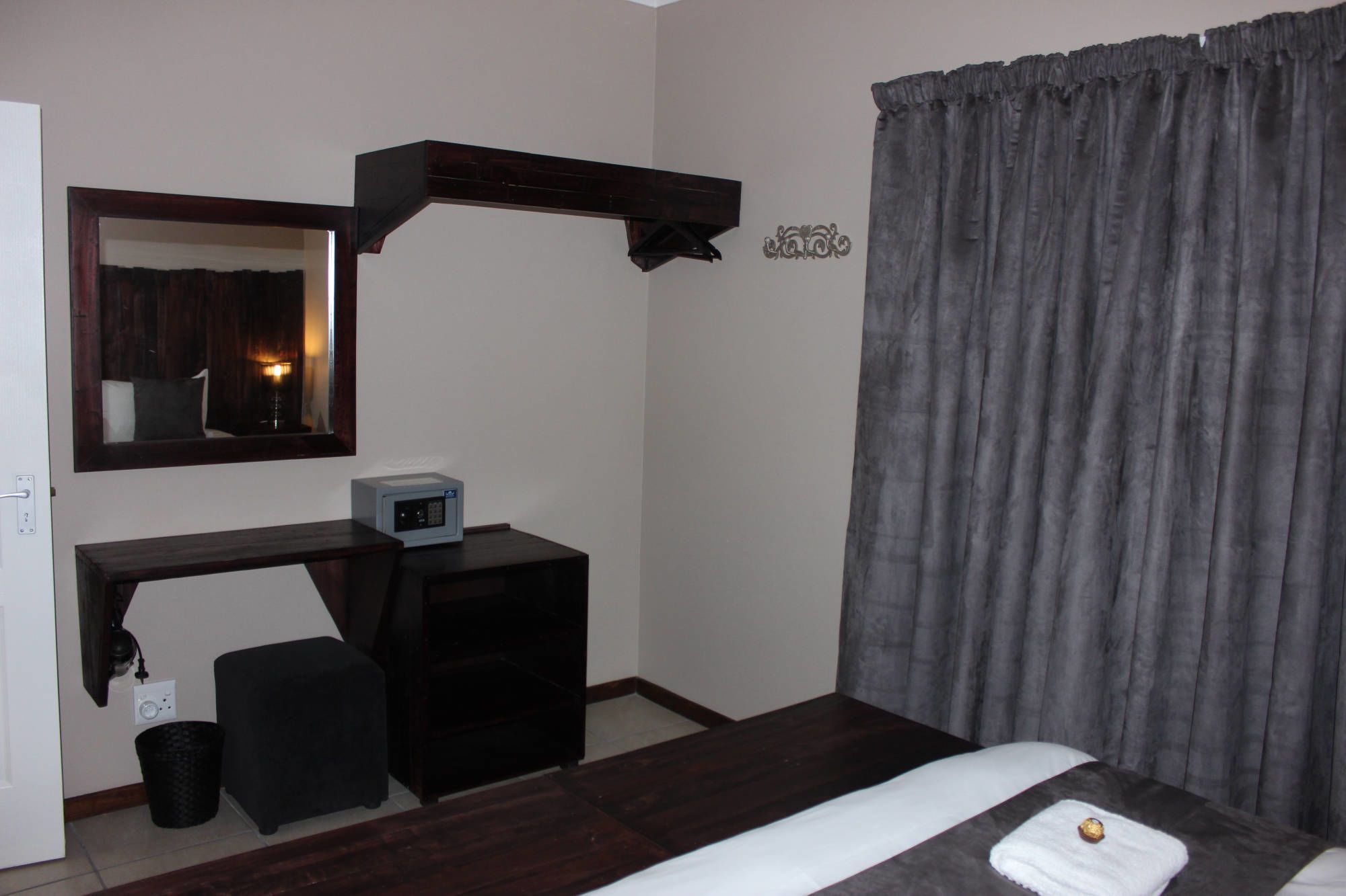 Habitación de hotel con cama, escritorio con computadora, silla, mesita, cesto de basura y cortina.