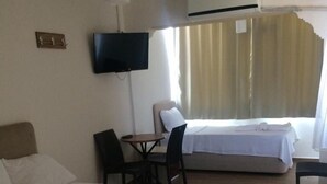 A hotel room with a bed, a desk, a chair, a TV, and a window with curtains. - Ev Otel (Çanakkale)