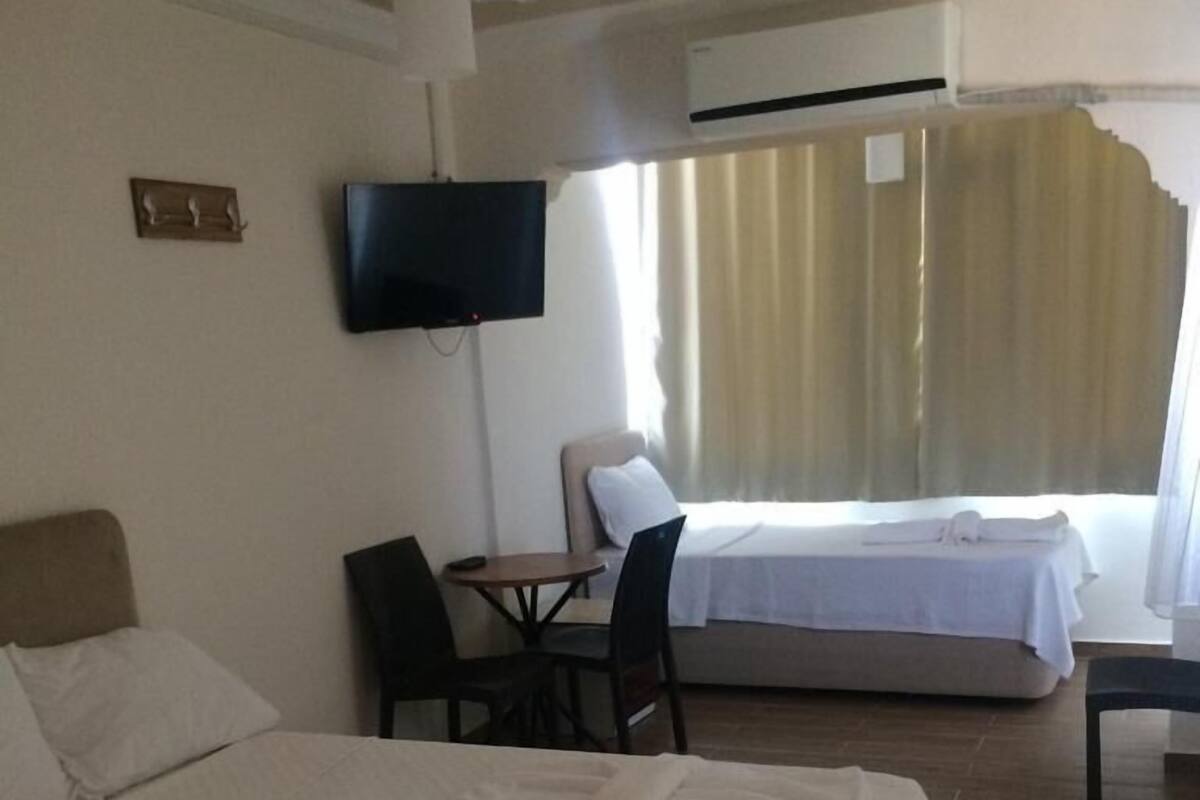 A hotel room with a bed, a desk, a chair, a TV, and a window with curtains.