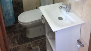 A bathroom with a toilet, a sink, a mirror, and a shower. - Ev Otel (Çanakkale)