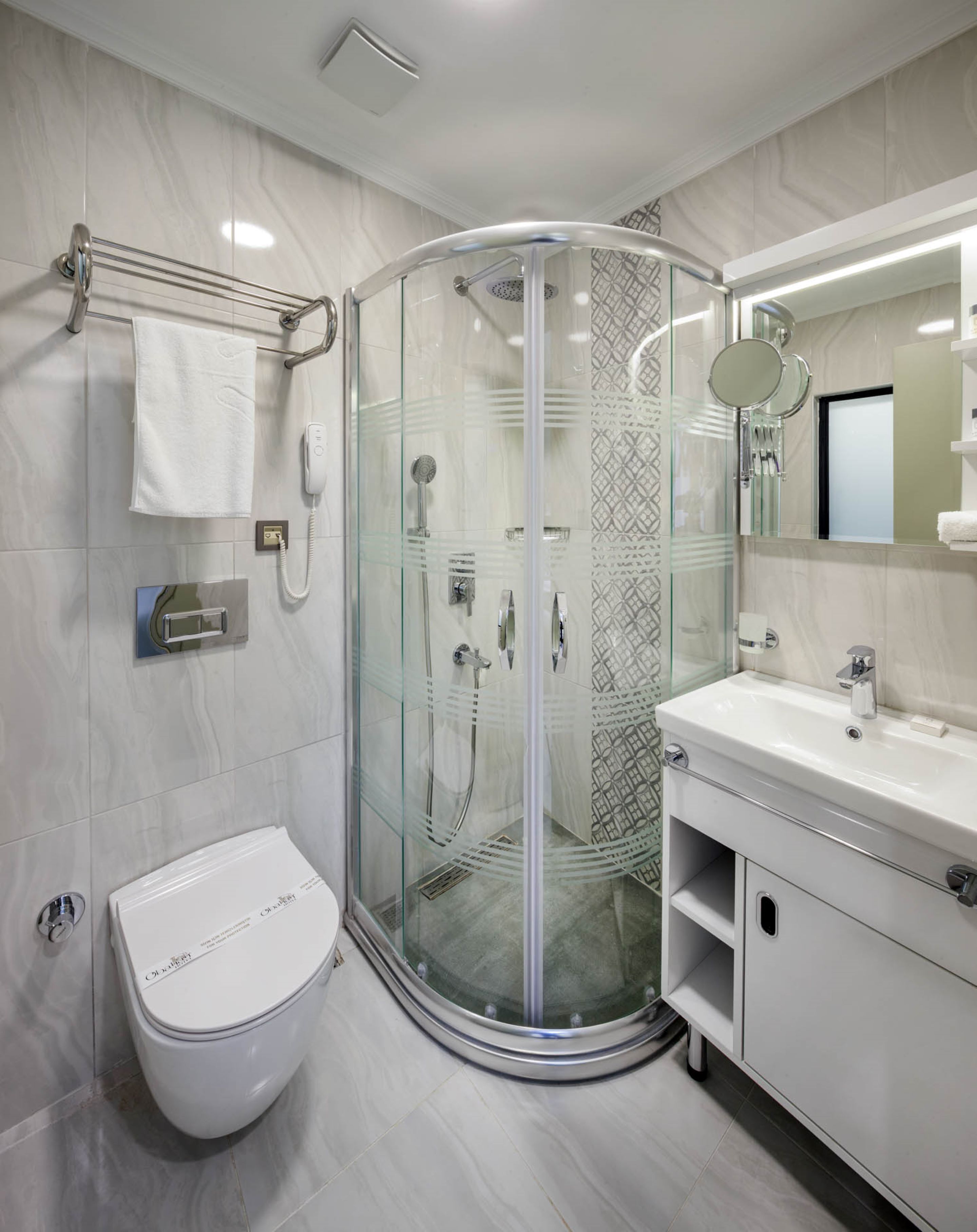 A modern bathroom with a glass-enclosed shower, a white toilet, a vanity with a mirror, and a towel rack.