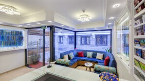 Un interior moderno con un separador de vidrio, un sofá azul con cojines estampados y una mesa de vidrio con un adorno decorativo.