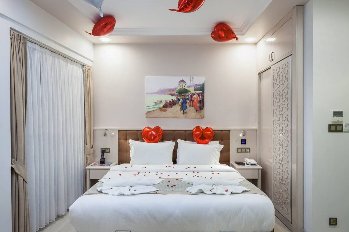 A hotel room with a large bed, a painting on the wall, and a ceiling with decorative lights.