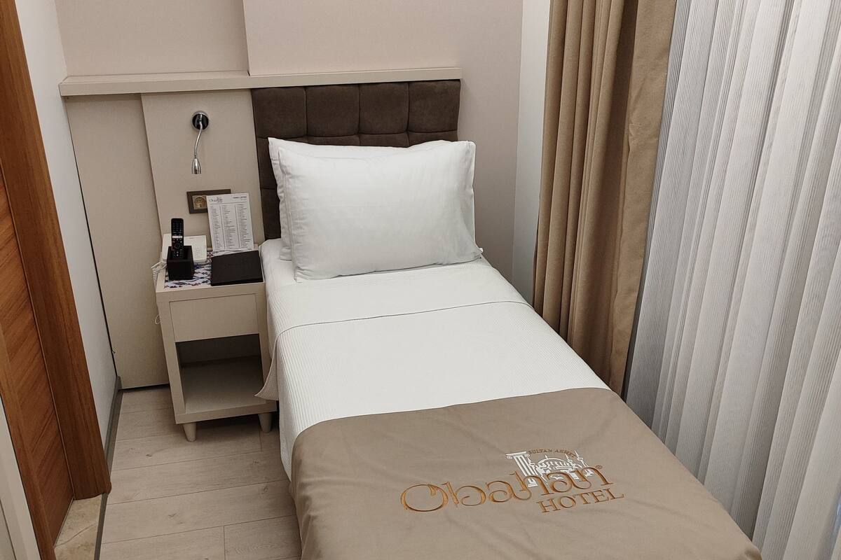 A hotel room with a bed, a nightstand, a bedside table, and a curtain.