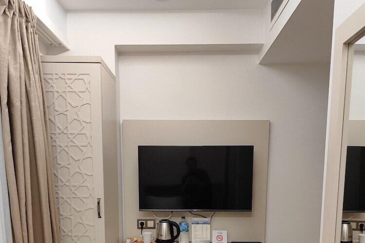 A hotel room with a bed, a desk with a television, a mini-fridge, and a coffee machine.