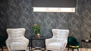 A room with two white armchairs, a small table, a potted plant, and a geometric-patterned wall. - Thr center (Curtea De Arges)