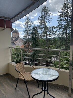 Un balcón con una silla de mimbre y una mesa de vidrio, con vistas a una iglesia y árboles.