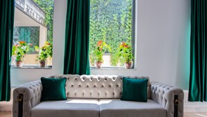 A tufted sofa with two green cushions, positioned in front of a window with potted plants. - Thr center (Curtea De Arges)