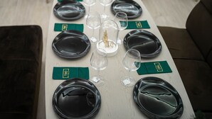 A dining table set with black plates, clear wine glasses, and green napkins with a logo. - Thr center (Curtea De Arges)