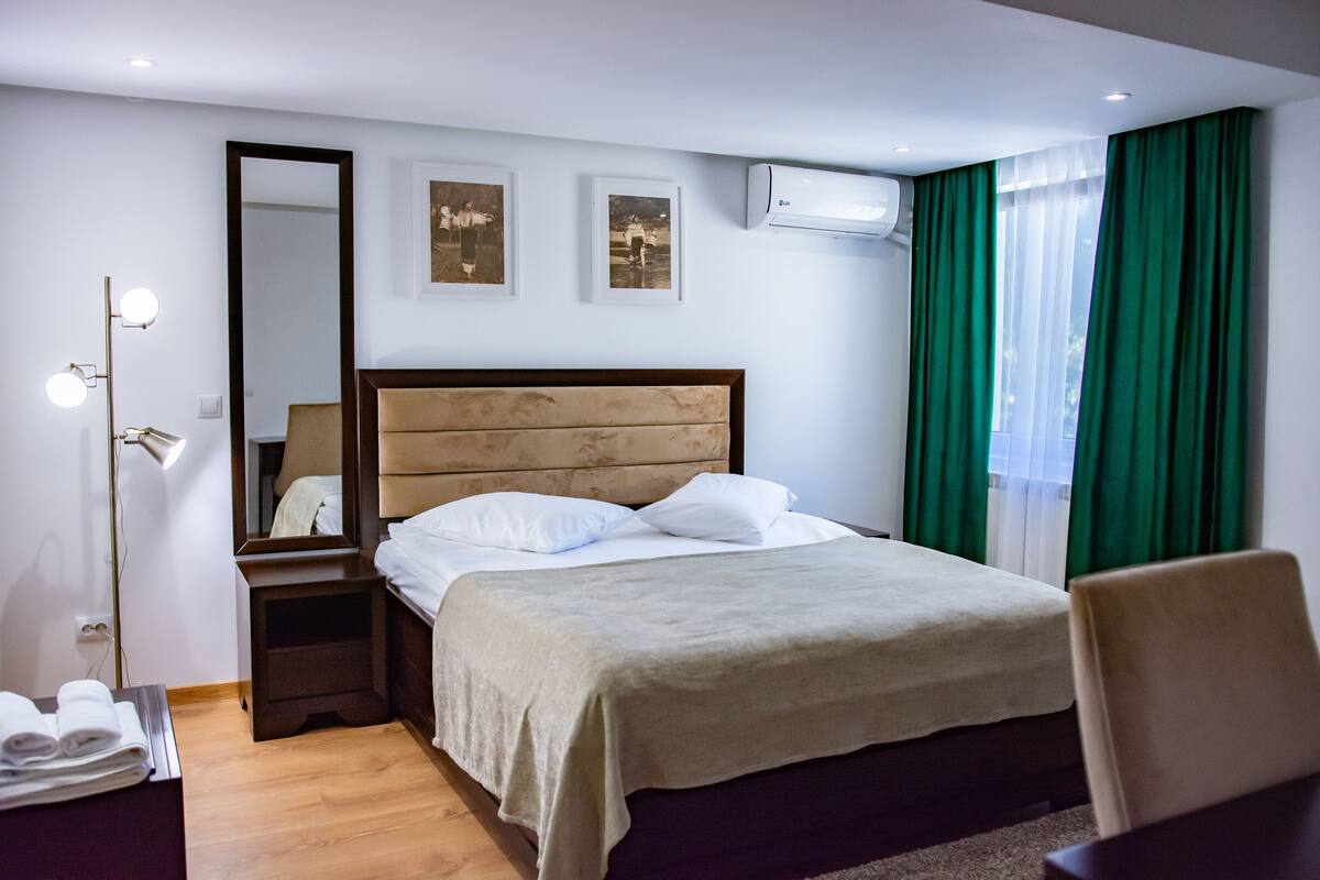 A hotel room with a bed, a nightstand, a mirror, and a wall-mounted air conditioner.