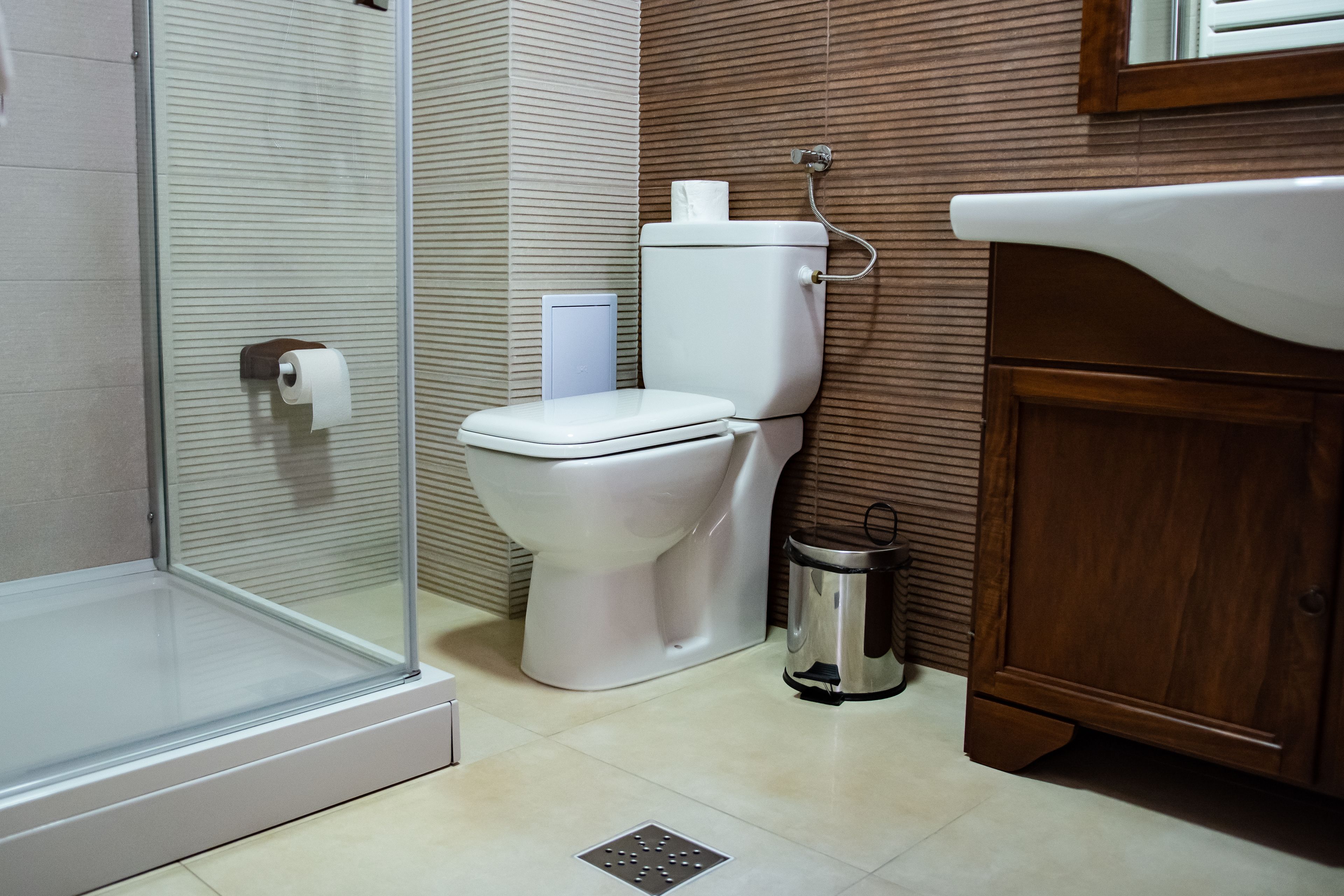 A bathroom with a toilet, a glass shower enclosure, a trash can, and a sink.