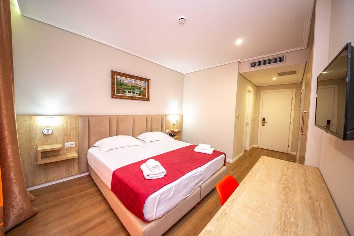 Una habitación de hotel con cama, mesita de noche, lámpara y un cuadro en la pared.