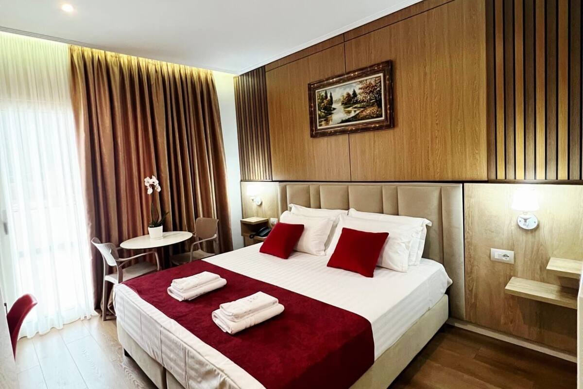 Habitación de hotel con una cama grande, una mesita de noche, una silla y una pequeña mesa con un jarrón de flores.