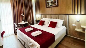 A hotel room with a large bed, a bedside table, a chair, and a small table with a vase of flowers.