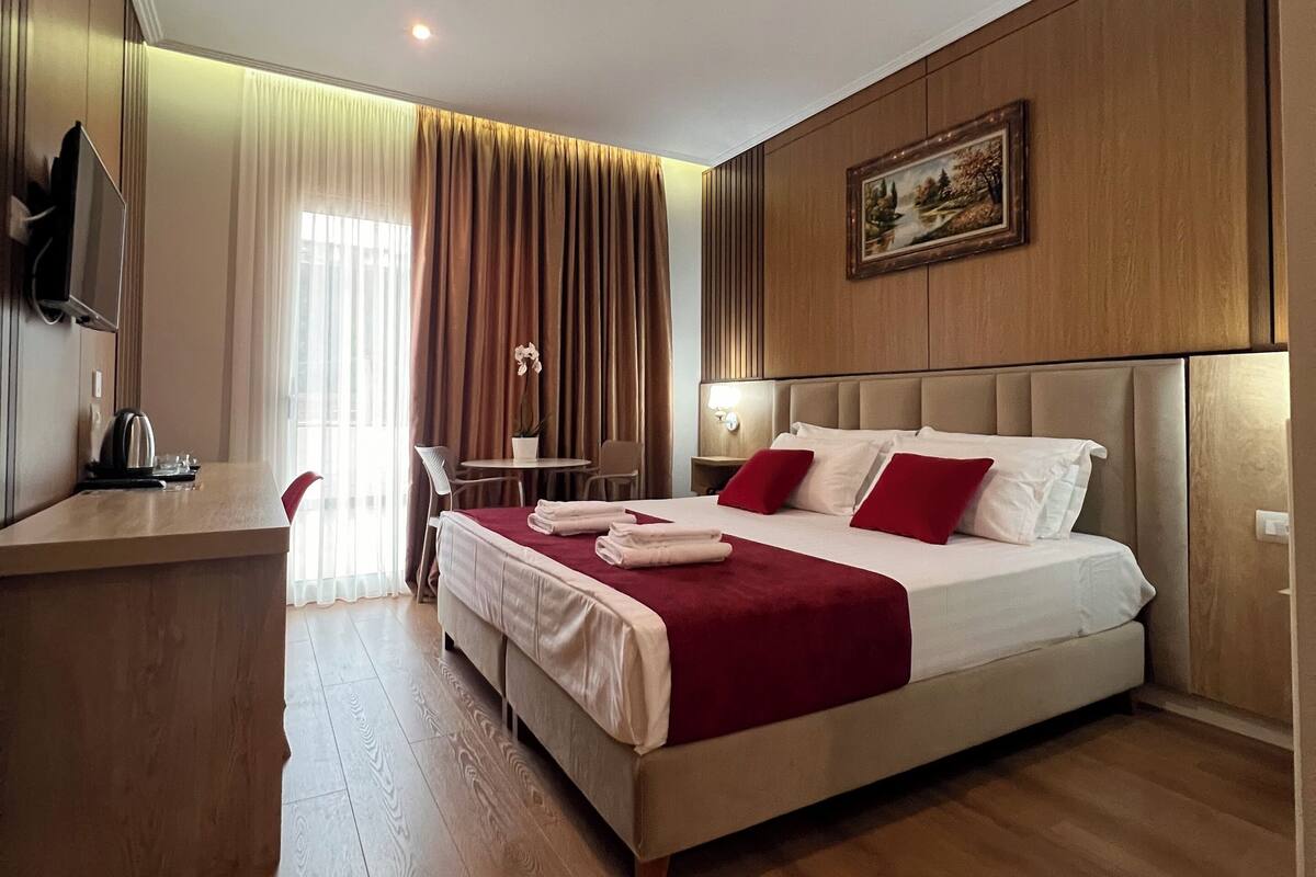 Habitación de hotel con una cama grande, un escritorio con una silla, un televisor montado en la pared y un cuadro sobre la cama.