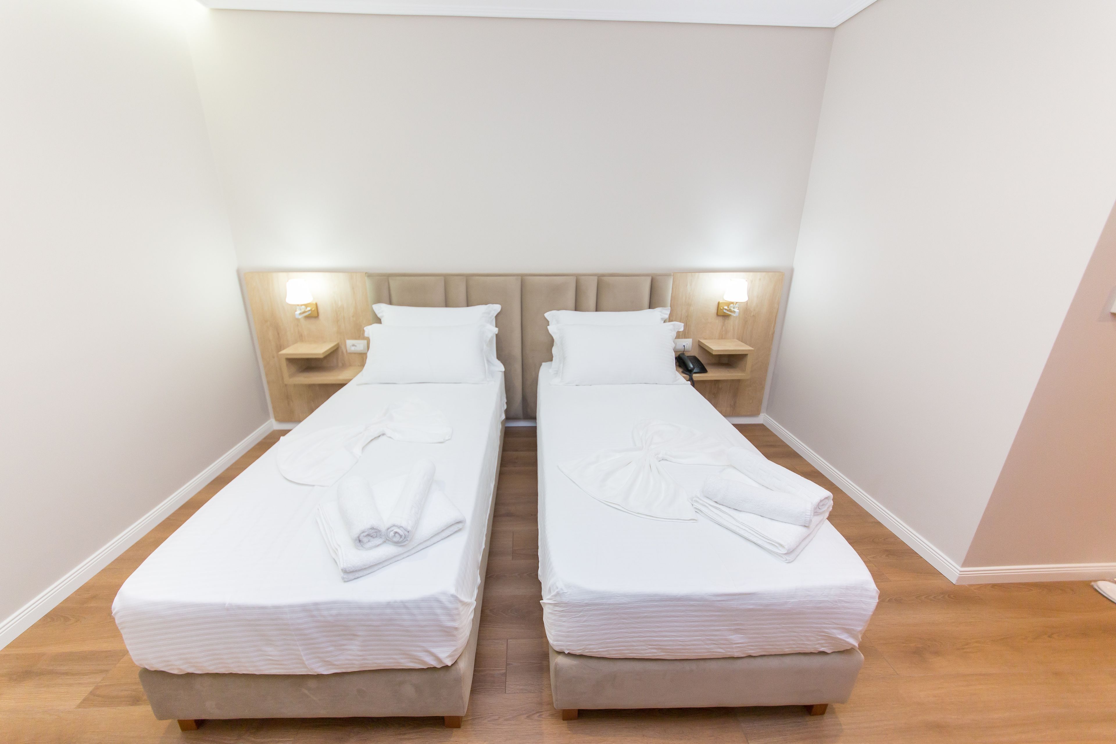 Camera doppia con due letti singoli, ognuno con cuscino, comodino e lampada.