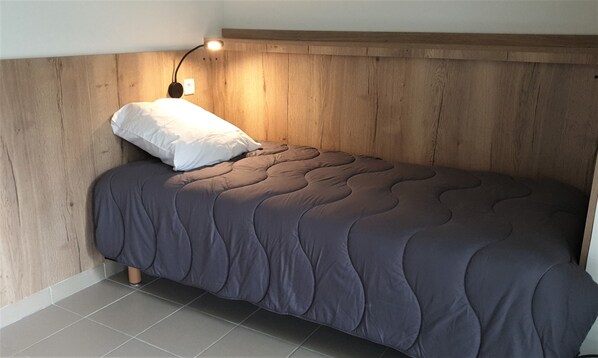 Una cama individual con cabecera de madera, almohada blanca y colcha gris oscuro.