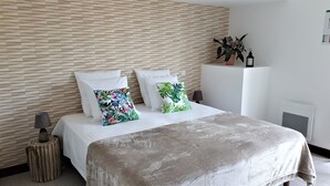 A bedroom with a bed, white pillows, a tropical-themed pillow, a potted plant, a black lantern, and a small wooden stool. - Hostel Les Terrasses du Roc (Saint-Andre-de-Roquepertuis)