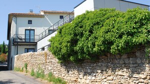 A two-story building with a stone wall and a lush green hedge in front. - Hostel Les Terrasses du Roc (Saint-Andre-de-Roquepertuis)