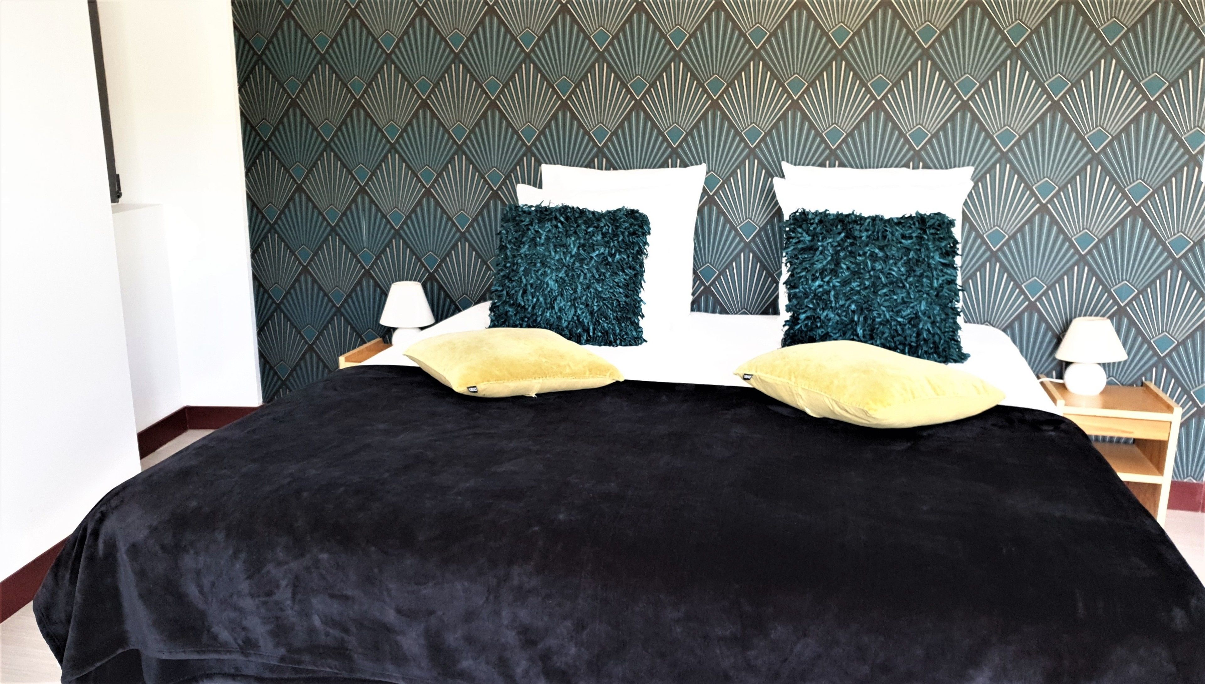 A bed with a black cover, two teal pillows, and two yellow pillows.