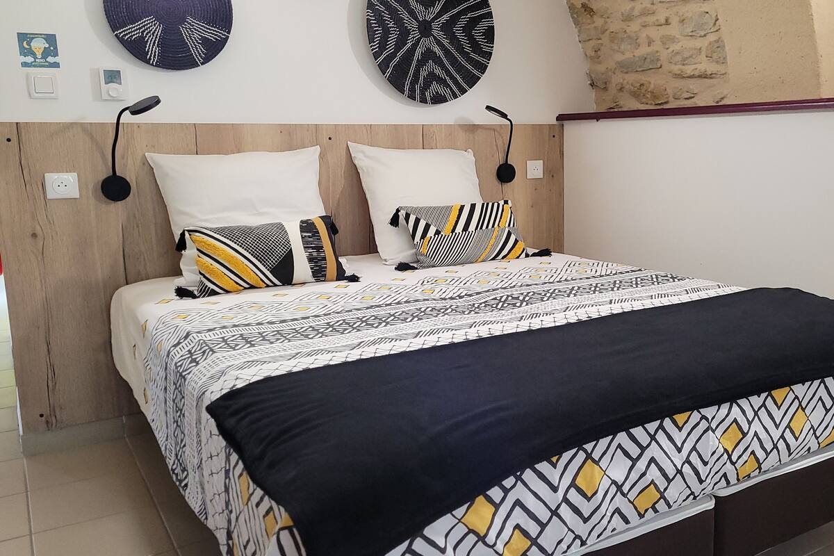 A bedroom with a wooden headboard, two bedside tables, a bed with patterned bedding, and wall-mounted decor.