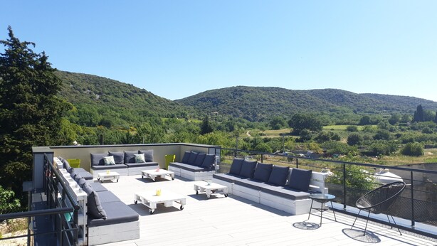 A rooftop terrace with outdoor seating, a view of a hilly landscape, and a clear sky. - Hostel Les Terrasses du Roc (Saint-Andre-de-Roquepertuis)