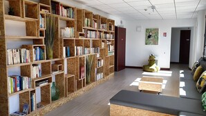 A library with wooden bookshelves filled with books, a green plant, and a statue. - Hostel Les Terrasses du Roc (Saint-Andre-de-Roquepertuis)