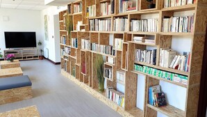 A library with wooden bookshelves filled with books, a television, and a potted plant. - Hostel Les Terrasses du Roc (Saint-Andre-de-Roquepertuis)