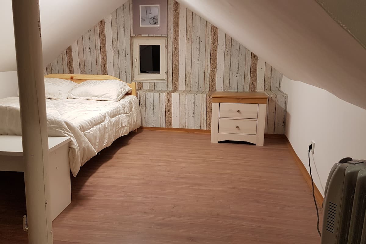 A small, cozy attic bedroom with a single bed, a nightstand, and a small window.