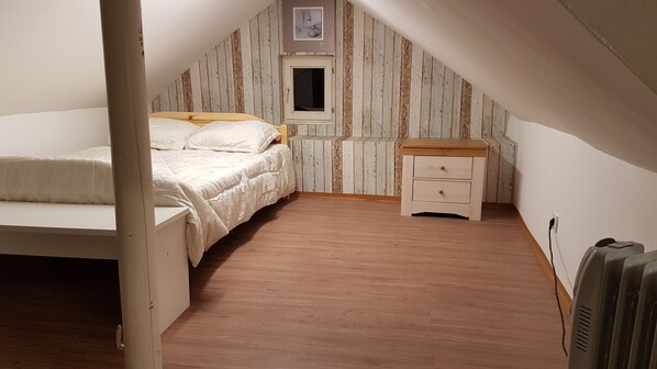 Un dormitorio acogedor en el ático, con una cama individual, una mesita de noche y un ventanal pequeño.