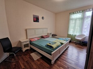 Un dormitorio con una cama, una silla, una mesita de noche y un ventanal con cortinas.