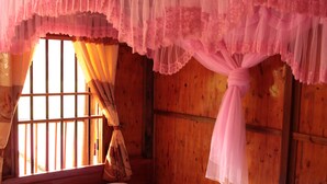 A wooden room with a bed, a window with bars, and pink curtains. - Tran Xuan Homestay - Hostel (Ba Be)