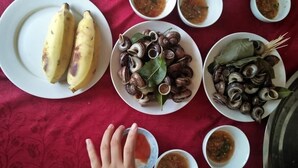A table with various dishes including bananas, snails, and bowls of soup. - Tran Xuan Homestay - Hostel (Ba Be)