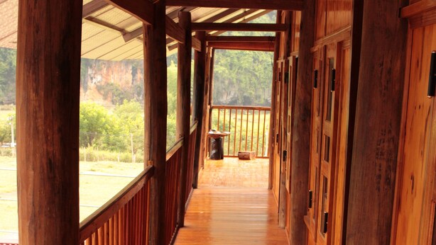 A wooden corridor with a railing, wooden doors, and a view of greenery outside. - Tran Xuan Homestay - Hostel (Ba Be)