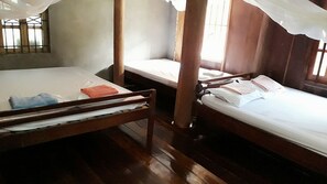 Una habitación con dos camas de madera, una ventana con rejas y suelo de madera.