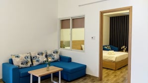 A small, modern room with a blue sofa, a wooden table, and a bed with a wooden headboard. - La Maison De Ruby Apartment (Da Nang)