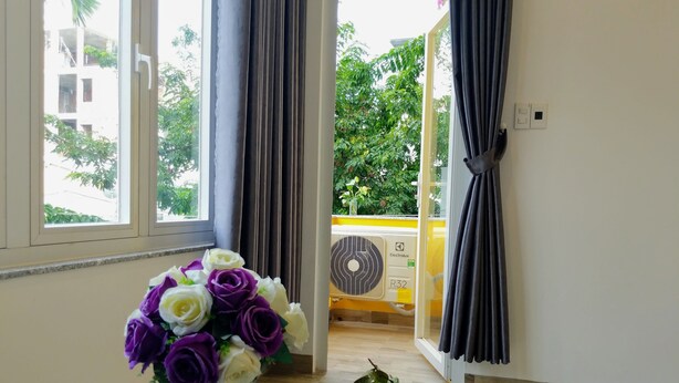 A room with a window, a white vase with purple and white flowers, and a plate with fruits. - La Maison De Ruby Apartment (Da Nang)