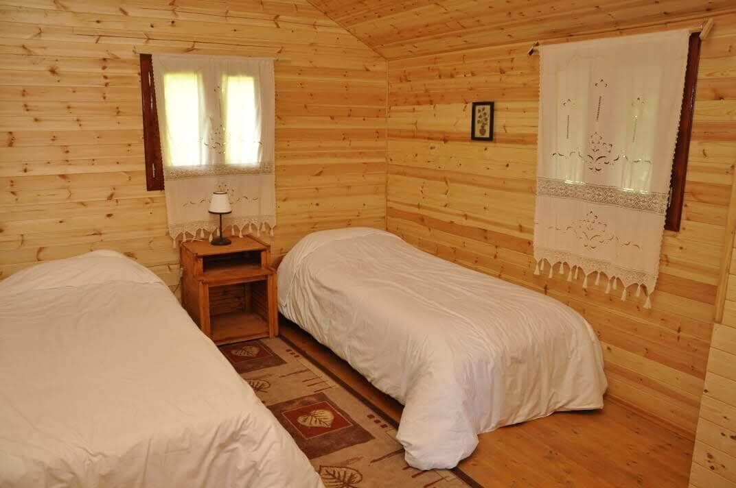 A cabin-style room with two single beds, a small wooden nightstand, and a window with curtains.
