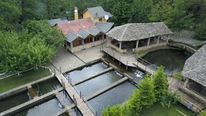 A rustic lodge with stone architecture, a small pond, and a wooden bridge. - Farma Sotira (Leskovik)