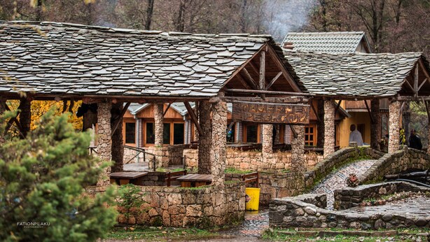 A rustic lodge with stone walls and wooden beams, featuring multiple rooms with large windows and a stone pathway leading to the entrance. - Farma Sotira (Leskovik)