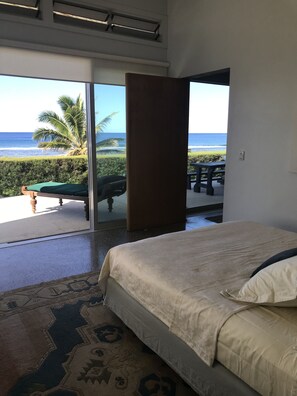 A bedroom with a bed, a view of the ocean, and a patio area with a table and chairs. - Coast Cook Islands - 3-Bedroom Beachfront Pool Villa (Rarotonga)