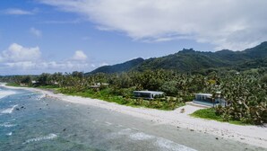A beachfront property with a clear view of the ocean, a sandy beach, and lush greenery. - Coast Cook Islands - 3-Bedroom Beachfront Pool Villa (Rarotonga)