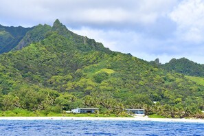 Ein Küstenblick mit einem Berg im Hintergrund, zwei Strandhäusern und wolkenlosem, blauem Himmel.
