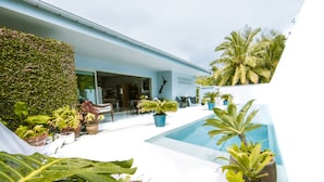 A modern outdoor pool area with potted plants and a seating area. - Coast Cook Islands - 3-Bedroom Beachfront Pool Villa (Rarotonga)
