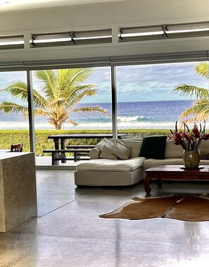 Een moderne woonkamer met een groot raam met uitzicht op een strand en de oceaan.
