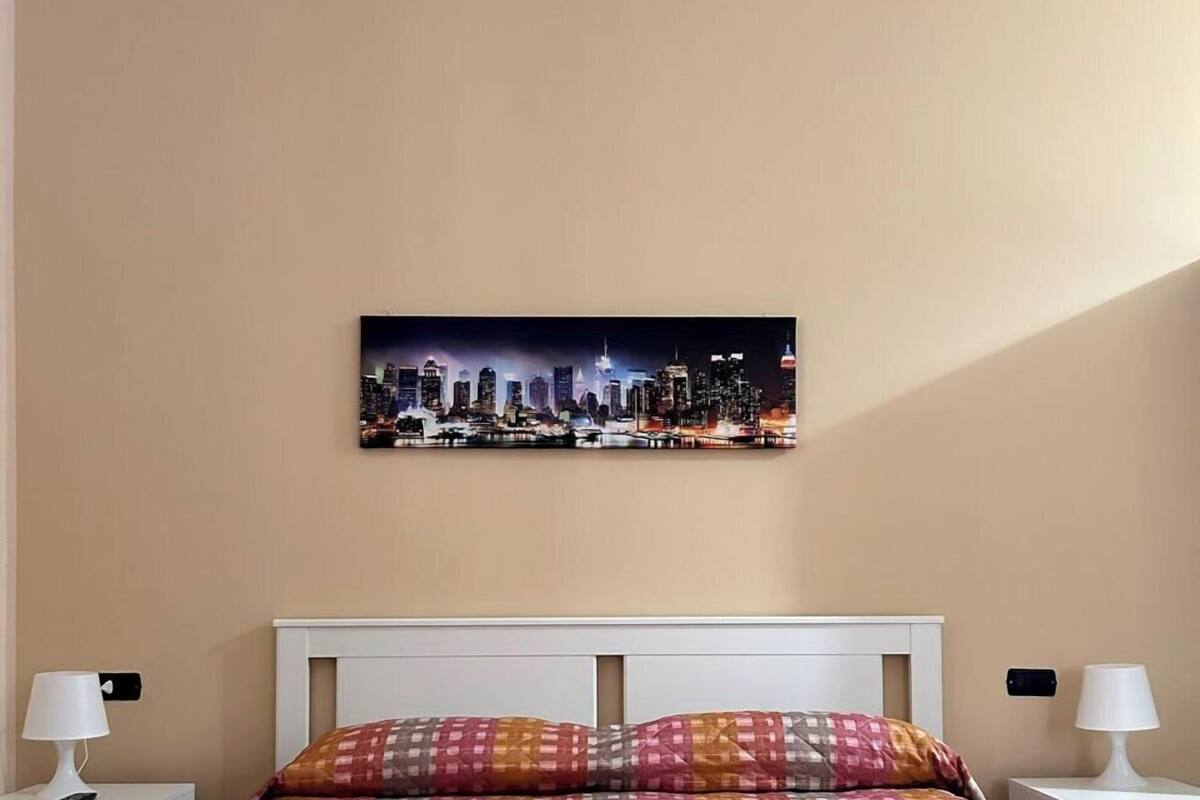 A hotel room with a bed, two pillows, a cityscape artwork on the wall, and two bedside lamps.