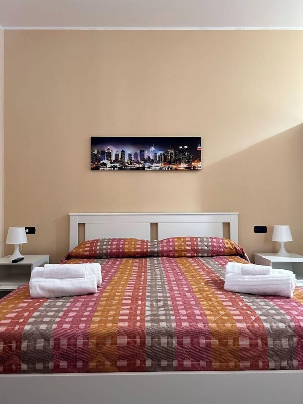 A hotel room with a bed, two pillows, a cityscape artwork on the wall, and two bedside lamps. - B&B Metropolitan RC (Reggio Calabria)