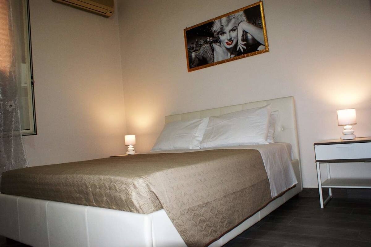 A neatly made bed with a beige blanket, two bedside tables with lamps, and a framed picture on the wall.